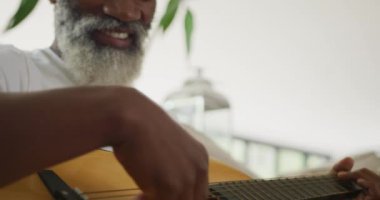 Üzgün Afrikalı Amerikalı son sınıf öğrencisinin gitar çalarkenki videosu. Emeklilik yaşam tarzı, ev konseptinde dijital olarak oluşturulmuş video ile zaman geçirme.