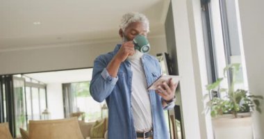 Afro-Amerikan son sınıf öğrencisinin kahve içip tablet kullandığı bir video. Emeklilik yaşam tarzı, ev konseptinde dijital olarak oluşturulmuş video ile zaman geçirme.