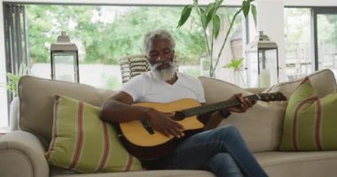 Üzgün Afrikalı Amerikalı son sınıf öğrencisinin gitar çalarkenki videosu. Emeklilik yaşam tarzı, ev konseptinde dijital olarak oluşturulmuş video ile zaman geçirme.