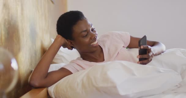 Αφροαμερικανή Γυναίκα Χαμογελά Και Χρησιμοποιεί Smartphone Μόνη Της Στην Κρεβατοκάμαρά — Αρχείο Βίντεο