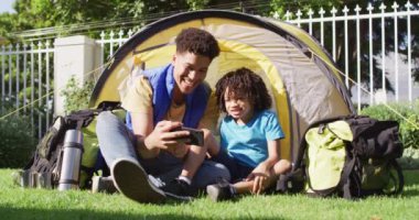 Mutlu melez adam ve oğlu bahçede akıllı telefon kullanıyor. ev hayatı, evde zaman geçirmek..