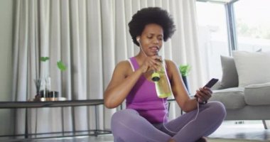 Mutlu Afrikalı Amerikalılar spor giyer, akıllı telefon kullanır, su içer. ev hayatı, evde boş zaman geçirmek..