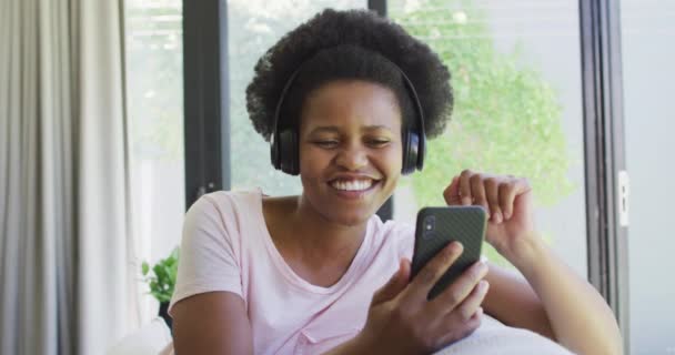 Счастливая Американка Африки Наушниках Сидит Диване Пользуется Смартфоном Бытовой Образ — стоковое видео