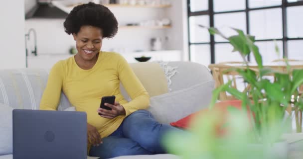 Mujer Afroamericana Feliz Sentado Sofá Utilizando Ordenador Portátil Teléfono Inteligente — Vídeos de Stock