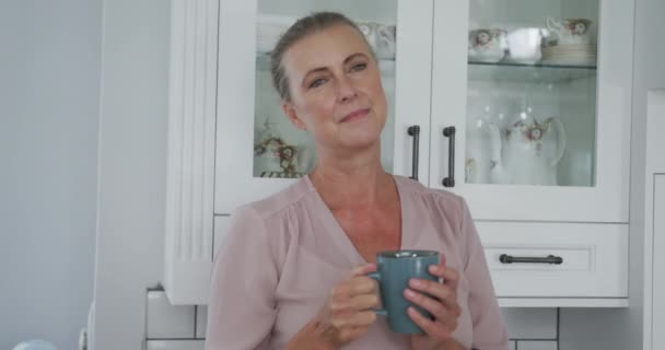 Старшая Белая Женщина Розовой Рубашке Кружкой Кофе Кухне Проводить Время — стоковое видео