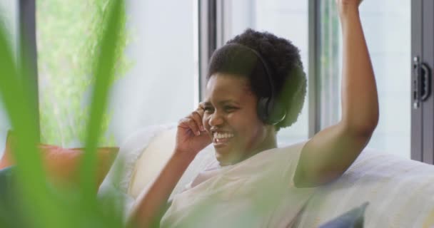 Χαρούμενη Αφροαμερικανή Που Φοράει Ακουστικά Καθισμένη Στον Καναπέ Οικιακή Ζωή — Αρχείο Βίντεο
