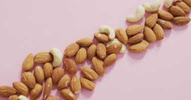 Pembe arka planda badem ve fındık videosu. Taze vejetaryen yemeği, bitki temelli diyet, sağlıklı beslenme konsepti.