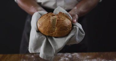 Aşçının siyah arka planda bir somun ekmeği tutuşu videosu. yemek ve yemek malzemeleri konsepti.