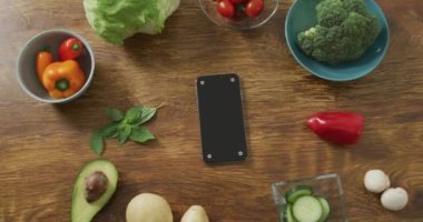 Sağlıklı meyve ve sebzelerin videosu ve ahşap arka planda akıllı telefon. Taze vejetaryen yemeği, bitki temelli diyet, sağlıklı beslenme konsepti.
