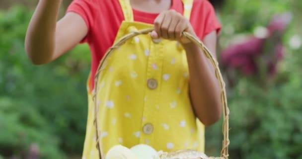 一个快乐的非洲裔美国女孩在花园里提着篮子和复活节彩蛋的动画 复活节 庆祝会及在户外度过美好时光 — 图库视频影像