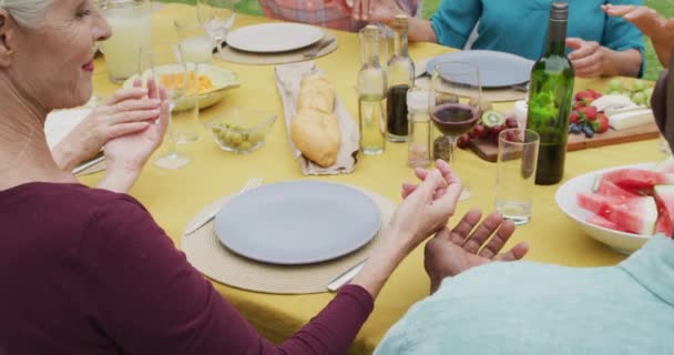 庭でお昼を食べながらお祈りをする 幸せな多様な女性と男性のシニア友達のアニメーション 退職生活 友人との時間を過ごすこと — ストック動画