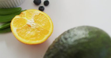 Beyaz arka planda taze avokado, portakal ve tohumların yakın çekim videosu. Füzyon yiyecekler, taze meyve ve sebzeler ve sağlıklı beslenme konsepti.