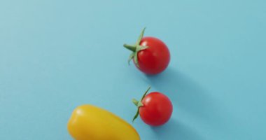 Mavi zemin üzerinde kopya alanı olan dört taze kiraz ve sarı domatesin yakın çekim videosu. Füzyon yiyecekler, taze sebzeler ve sağlıklı yeme konsepti.