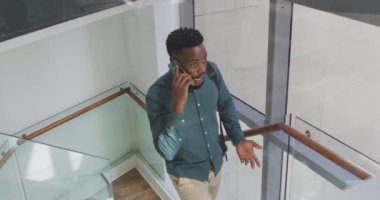 Afrika kökenli Amerikalı iş adamı akıllı telefondan konuşuyor ve yaratıcı ofiste yürüyor. Yaratıcı ofiste iş ve finans.