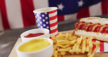 Tahta bir yüzey üzerinde hardallı, ketçaplı ve patates kızartmalı sosisli sandviç videosu. Yemek, yemek ve yemek malzemeleri..