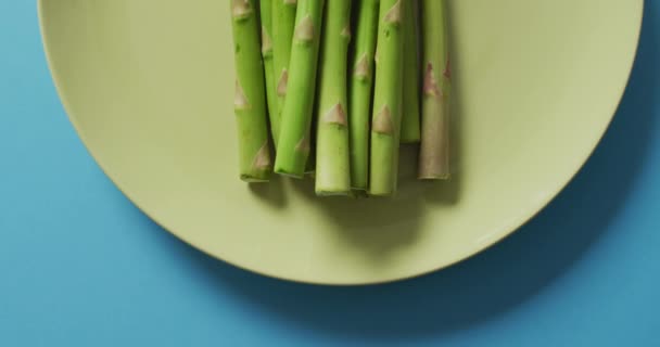 青い背景の上に緑のプレート上の新鮮なアスパラガスのビデオ 融合食品 新鮮な野菜や健康的な食事の概念 — ストック動画