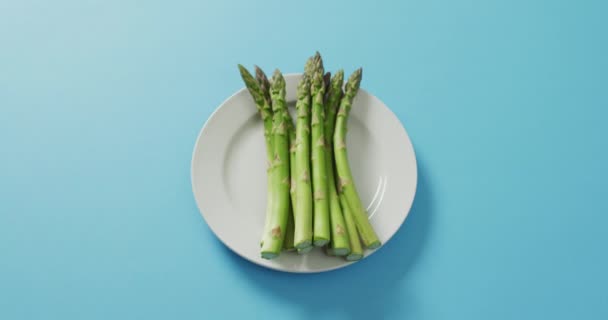蓝色背景的白色盘子上新鲜芦笋的视频 融合食物 新鲜蔬菜及健康饮食概念 — 图库视频影像
