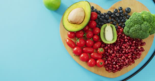 在蓝色背景的心形木板上的听诊器和新鲜水果蔬菜的视频 融合食物 新鲜蔬菜及健康饮食概念 — 图库视频影像