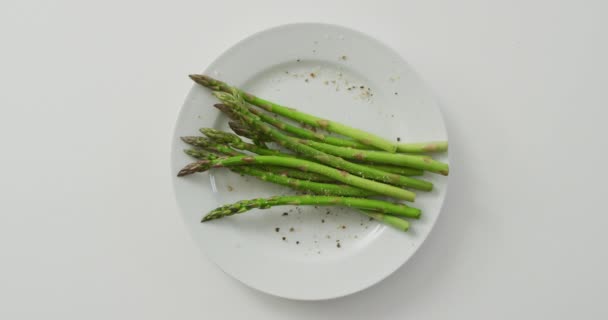白い背景に白いプレートの上に新鮮なアスパラガスの茎のビデオ 融合食品 新鮮な野菜や健康的な食事の概念 — ストック動画