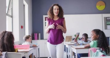 Kafkasyalı bayan öğretmen ve çeşitli öğrencilerin sınıfta ders çalışmalarının videosu. İlkokul eğitimi ve öğretmenlik mesleği.