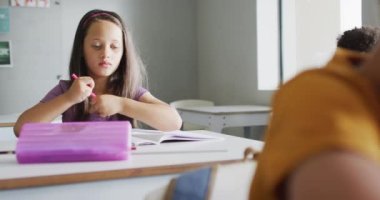 Video of caucasian girl sitting at desk in classroom. primary school education and learning concept.