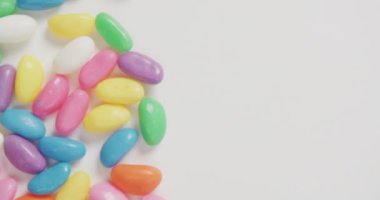 Beyaz zemin üzerinde fotokopi alanı olan çok renkli şekerlerin yakın çekim videosu. Füzyon yiyecek ve tatlı konsepti.
