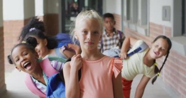 Video of happy caucasian girl and diverse pupils at school corridor. primary school education and learning concept.