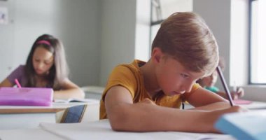 Video of focused caucasian boy sitting at desk in classroom. primary school education and learning concept.