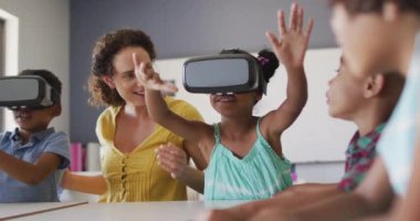 Kafkasyalı mutlu kadın öğretmen videosu ve VR kulaklık takan çeşitli öğrenciler. İlkokul eğitimi ve öğretmenlik mesleği.