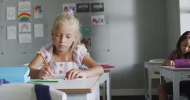 Video of focused caucasian girl sitting at desk in classroom. primary school education and learning concept.