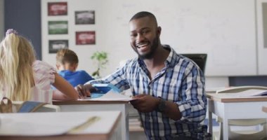 Dersler sırasında öğrencilere yardım eden mutlu Afro-Amerikan erkek öğretmenin videosu. İlkokul eğitimi ve öğretmenlik mesleği.