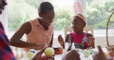 African american mother and daughter painting easter eggs together at home. easter holiday spirit and joy concept