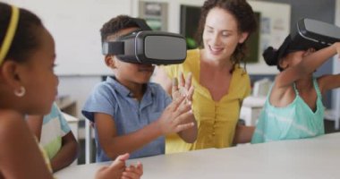 Kafkasyalı mutlu bayan öğretmen ve VR kulaklık takan Afrikalı Amerikalı öğrencilerin videosu. İlkokul eğitimi ve öğretmenlik mesleği.