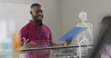 Anatomi dersi sırasında farklı sınıflardan öğrencileri olan mutlu bir Afrikalı Amerikan öğretmeninin videosu. İlkokul eğitimi ve öğretmenlik mesleği.