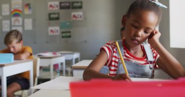 Sınıfta masasında oturan düşünceli Afrikalı Amerikalı kızın videosu. İlkokul eğitimi ve öğrenme kavramı.