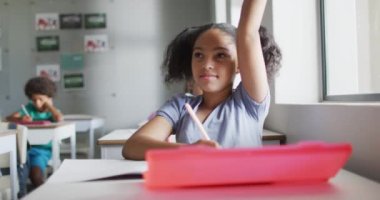 Video of happy biracial girl raising hand during lesson in classroom. primary school education and learning concept.