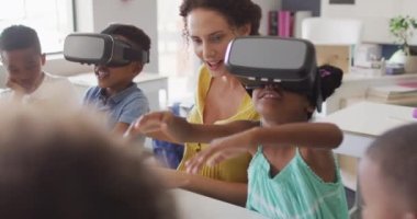 VR kulaklık takan farklı sınıftan öğrencilerin olduğu mutlu beyaz kadın öğretmen videosu. İlkokul eğitimi ve öğretmenlik mesleği.