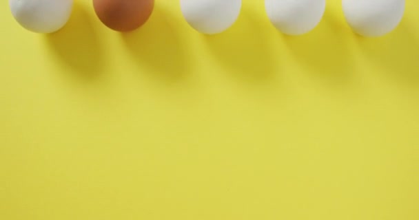 黄色の背景に1個の茶色と4個の白い卵の列のビデオ 融合食品 ベーキング 卵とイースターの概念 — ストック動画