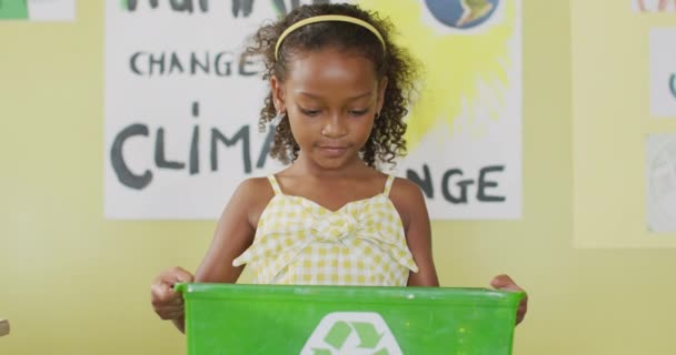 教室でリサイクルのシンボルが付いた箱を持っている幸せなアフリカ系アメリカ人の少女のビデオ 小学校教育と学習の概念 — ストック動画