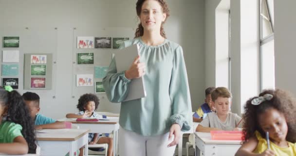 Wideo Szczęśliwej Białej Nauczycielki Trzymającej Laptopa Klasie Różnorodnych Uczniów Szkolnictwo — Wideo stockowe