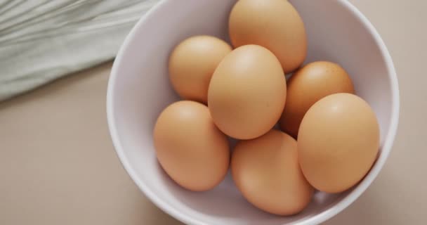 ベージュの背景に卵と卵泡立て器で白いボウルのオーバーヘッドビューのビデオ 融合食品 ベーキング 卵とイースターの概念 — ストック動画