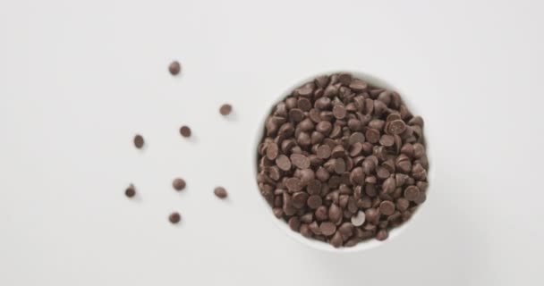 白い背景の上にボウルに複数のチョコレートチップのオーバーヘッドビューのビデオ 融合食品チョコレートとお菓子のコンセプト — ストック動画