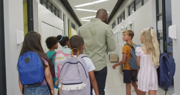 非洲裔美国男教师和各种各样的学生在学校大厅里散步的视频 小学教育和教学专业 — 图库视频影像