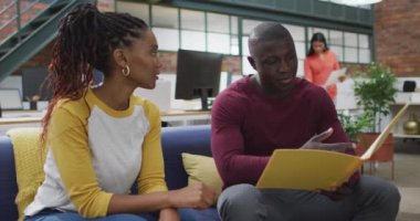 Mutlu Afro-Amerikan kadın ve erkek iş arkadaşları ofiste dosya okuyor. Yaratıcı bir şirkette çalışıyorum..