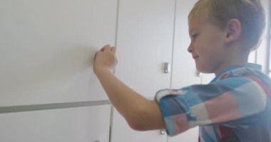 Dolabı kapatıp okulda gülümseyen beyaz bir çocuğun videosu. ilköğretim, bilgi ve öğrenme kavramı.