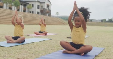 Okulun önündeki minderlerde yoga yapan farklı kızların videosu. İlkokul eğitimi, spor ve egzersiz konsepti.