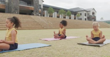 Okulun önündeki minderlerde yoga yapan farklı kızların videosu. İlkokul eğitimi, spor ve egzersiz konsepti.