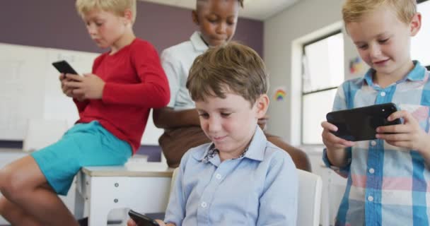 不同的男孩坐在课桌前 在智能手机上玩游戏的视频 小学教育 知识和学习概念 — 图库视频影像