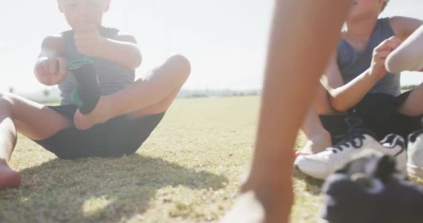 芝生の上に座って靴下を脱ぐ幸せな多様な男の子のビデオ 小学校教育 スポーツ — ストック動画