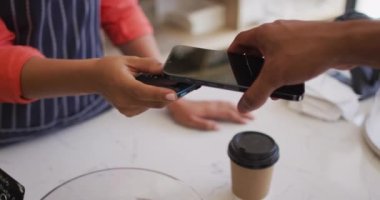 Video of hands of biracial man paying with smartphone for coffee. coffee and bistro shop, running small independent business.